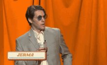 a man in a suit and sunglasses holds a glass in front of a sign that says " jerma "