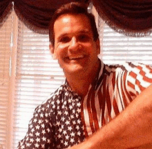 a man wearing an american flag shirt is smiling and looking at the camera .