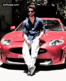 a man is leaning against a red sports car with the license plate mh