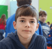 a young boy wearing a blue hoodie is looking at the camera