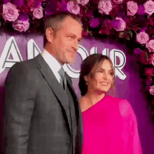 a man in a suit and tie stands next to a woman in a pink dress in front of a sign that says amour