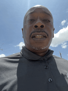 a man wearing a black shirt with buttons on it looks at the camera