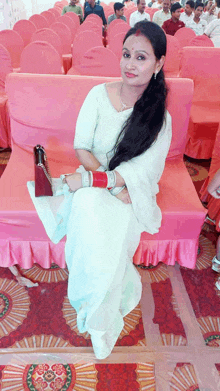 a woman in a white saree sits on a pink couch