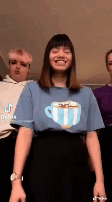 a woman wearing a blue t-shirt with a cup of coffee on it is standing next to two other women .