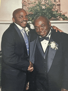 two men in tuxedos are posing for a picture and one has his arm around the other 's shoulder