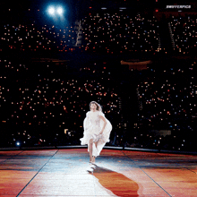 a woman in a white dress is running on a stage with swifterpics written on the bottom of the image