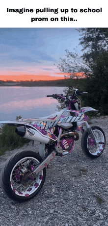 a pink and white dirt bike is parked on a gravel road near a lake .