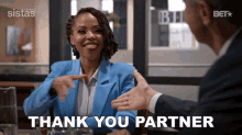 a woman in a blue jacket is sitting at a table with a man in a suit and says thank you partner