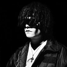 a black and white photo of a man with dreadlocks and a cross necklace