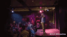 a man stands on a stage in front of a crowd with the hashtag #iduh #showtime