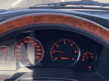 a close up of a car 's dashboard with a wooden steering wheel and a speedometer that shows a speed of 220