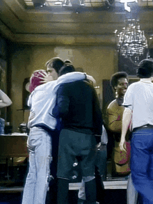 a group of people are hugging each other in a room with a chandelier .