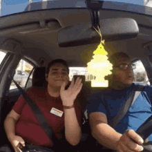 a man and woman are sitting in a car with a tree air freshener hanging from the rear view mirror