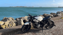 a black and white motorcycle is parked on a gravel road by the ocean