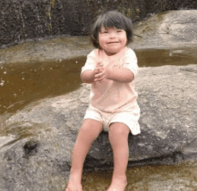 a little girl is sitting on a rock in front of a stream