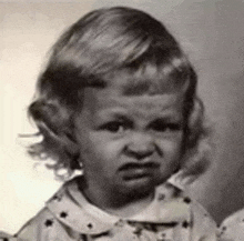 a black and white photo of a little girl with an angry look on her face .