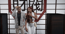 a man and a woman are standing in front of a wall with chinese writing on it