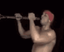 a shirtless man in a red bandana is playing a clarinet .