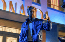 a man in a blue jacket is giving a thumbs up in front of a building that says ona