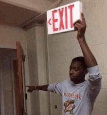 a man in a maryland shirt is holding an exit sign over his head .