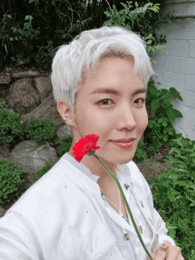 a young man with white hair is holding a red flower in front of his face