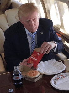 a man in a suit and tie is sitting at a table eating a mcdonald 's hamburger