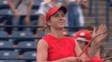 a woman in a red shirt is holding a tennis racquet on a tennis court while a crowd applauds .