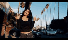 a woman is standing on a street with palm trees in the background and making a peace sign .