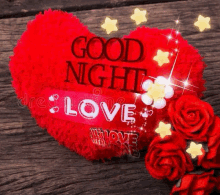 a red heart shaped pillow with the words `` good night love '' written on it is surrounded by red roses .