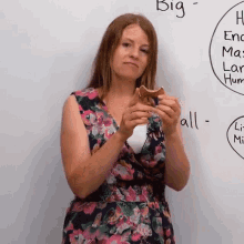 a woman in a floral dress is holding a piece of food in front of a whiteboard that says big