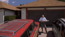 a man in a white shirt is holding a tray in front of a red suv in front of a house