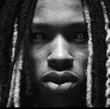 a close up of a person 's face with dreadlocks in a black and white photo .