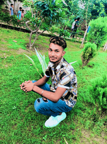 a young man is kneeling down in the grass and smiling at the camera