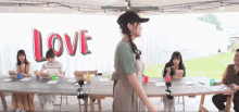 a group of people are sitting at tables under a tent with the word love written on the wall behind them