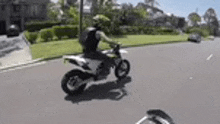 a man is riding a dirt bike down a street in a residential area .