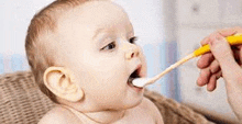 a baby is being fed with a spoon in his mouth .