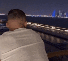 a man in a white shirt looks out over a body of water at night