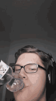 a man wearing glasses and headphones is drinking from a bottle