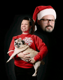 a man wearing a santa hat is holding a woman holding a pug dog