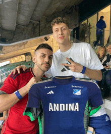 two men standing next to a blue andina shirt