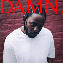 a man in a white shirt is standing in front of a red brick wall with the word damn in red letters