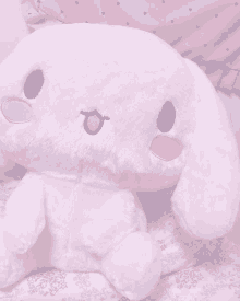 a white stuffed animal with a blue eye is sitting on a bed next to a pink pillow