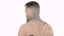 a man with a beard is standing in front of a white background with his back to the camera .