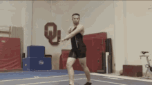 a man is doing a trick on a gym floor with a letter q on the wall in the background