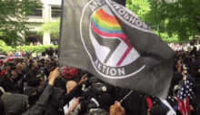 a large group of people are holding a black flag with a rainbow in the middle .