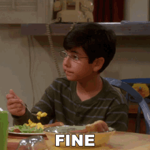 a young boy sitting at a table with a bowl of food and the word fine written on the table