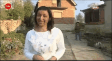 a woman with red paint on her face is standing in front of a house with a pink logo on the bottom right