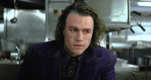 heath ledger is playing the joker in a purple suit and tie .