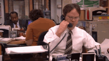 a man in a white shirt and tie is talking on a phone with a nbc sign in the background