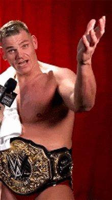 a man without a shirt is holding a microphone and a wrestling belt .